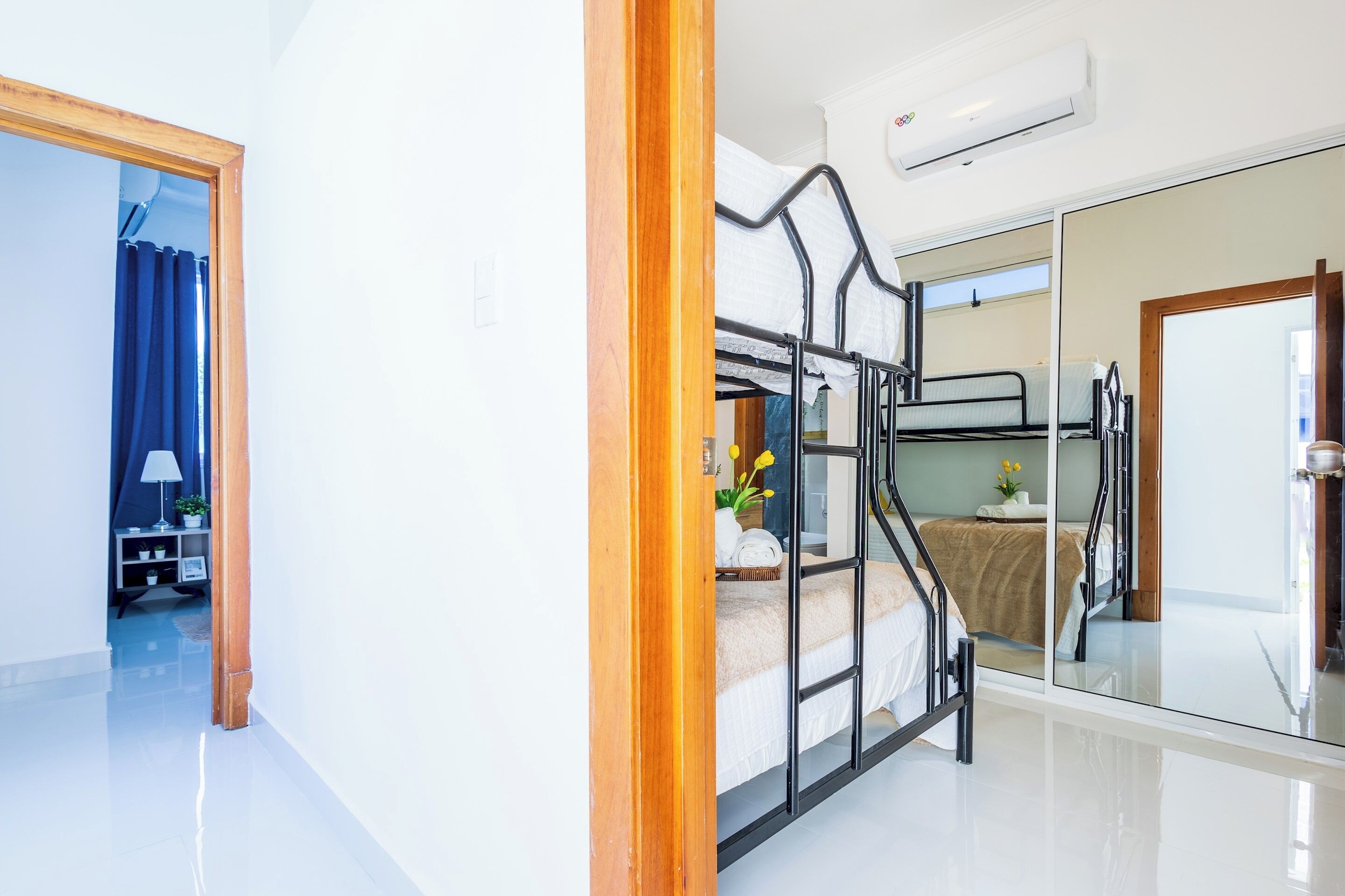 Une chambre d’hôtel moderne avec un lit superposé, une cloison en verre, un miroir et une porte en bois.