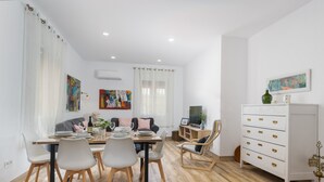 Un espace repas moderne avec une table dressée pour quatre personnes, un canapé, un téléviseur et un meuble blanc avec des tiroirs.