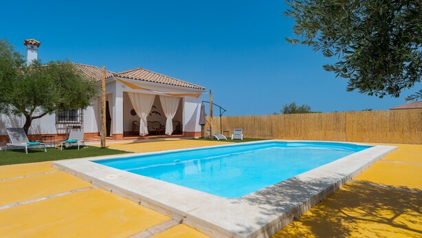 Une piscine avec une terrasse carrelée, un espace extérieur aménagé et couvert, et une clôture en bois.