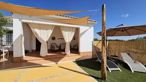 Un espace extérieur abrité, aménagé avec des chaises et une table, délimité par une clôture en bois et agrémenté d’une pergola avec des rideaux blancs.