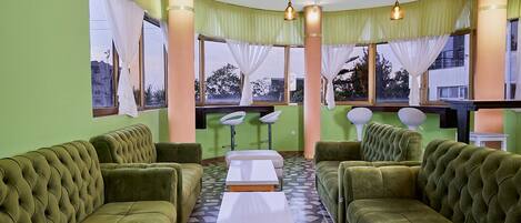 Una habitación con sofás tapizados en verde, una mesa blanca en el centro y ventanas grandes con cortinas.