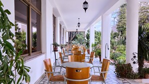 A covered outdoor seating area with tables and chairs, surrounded by potted plants and a view of greenery. - Garden Hills Hotel (Addis Ababa)