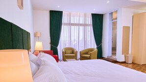 A hotel room with a large bed, two armchairs, a lamp, and a view of the outdoors through sheer curtains. - Garden Hills Hotel (Addis Ababa)