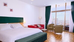 A hotel room with a large bed, a red sofa, two armchairs, and a view of the city through large windows. - Garden Hills Hotel (Addis Ababa)