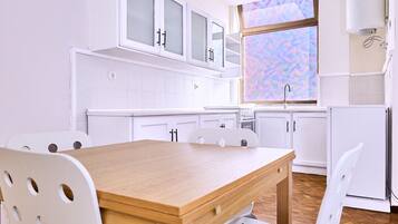 A modern kitchen with white cabinets, a wooden table, and a window with a colorful view.