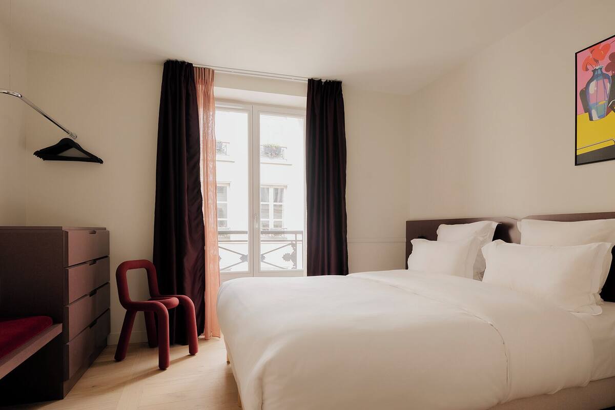 A hotel room with a bed, a desk, a chair, and a window with curtains.