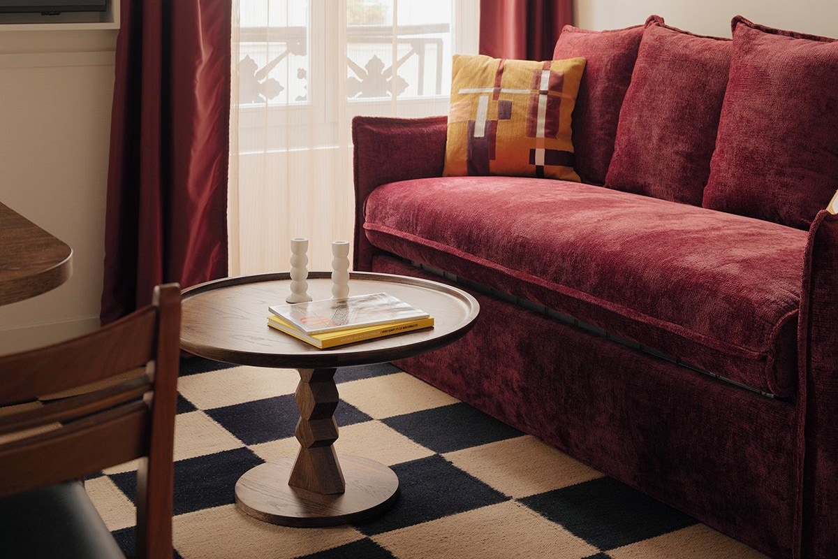 Una sala acogedora con un sofá rojo, una mesa redonda con libros y una alfombra estampada.