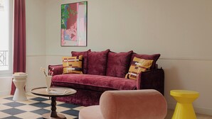 A living room with a checkered floor, a pink sofa, a yellow stool, and a pendant light. - Edgar Suites - Lemercier  (Paris)