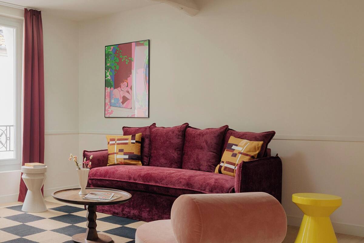 A living room with a checkered floor, a pink sofa, a yellow stool, and a pendant light.