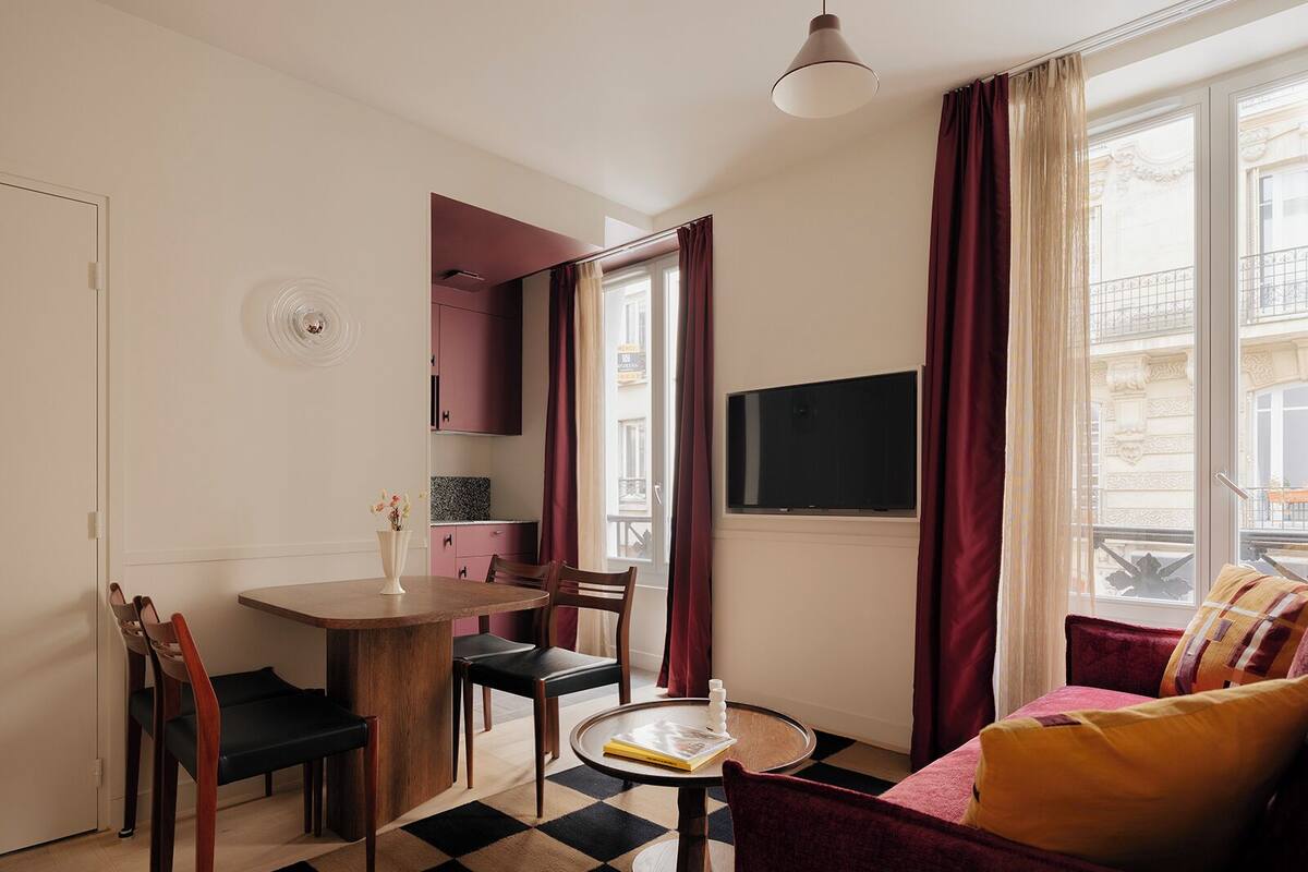 A compact living space with a dining area, a sofa, a TV, and a window with curtains.