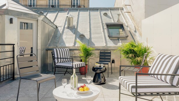 A rooftop terrace with a table set for two, two chairs, a small potted plant, and a bottle. - Edgar Suites - Lemercier  (Paris)