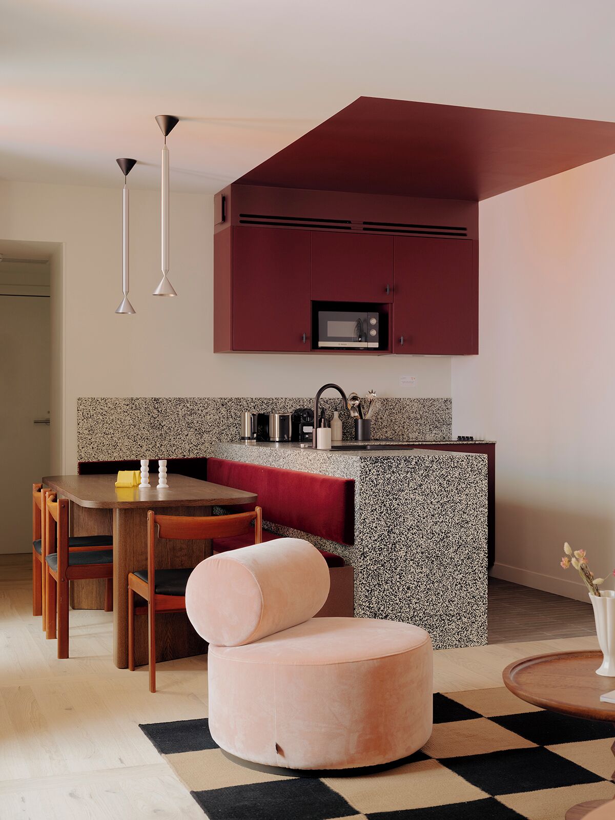 Una cocina moderna con microondas, una mesa de comedor con sillas y un pouf rosa.