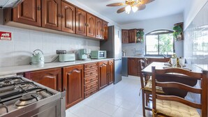 Une cuisine avec des meubles de rangement en bois, une cuisinière à gaz, un four à micro-ondes et un ventilateur de plafond.