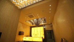 A modern hotel room with a large wooden reception desk, a chandelier, and a large window. - MVR Grand Hotel (Kanpur)