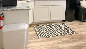 Una cocina compacta con armarios blancos, un refrigerador negro y un tapete estampado.