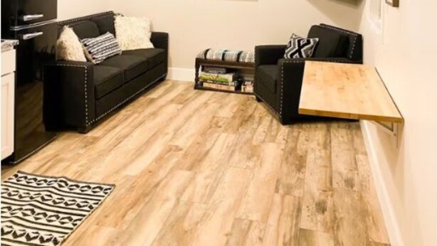 Ein Loft-Wohnzimmer mit freiliegenden Holzbalken, einer schwarzen Couch, einem Holztisch und einem flachbildfernseher an der Wand.
