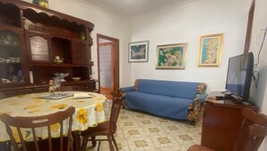 A dining area with a round table, chairs, a blue sofa, and a television. - CASA DONNA CONCETTA (Positano)