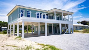 A two-story beachfront house with a balcony, a covered patio, and a sandy beach in the background. - New Construction! Dogs OK, Elevator, Direct Beach Access! (Eastpoint)