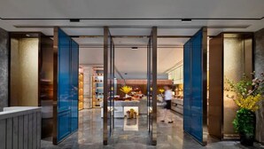 Un moderno vestíbulo de hotel con un separador de vidrio, una recepción y un área de comedor al fondo.