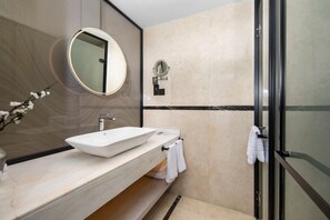 Egy modern fürőszoba, melyben egy nagy tükör, egy mosdókagyló és egy üvegfalas zuhanyzó található.