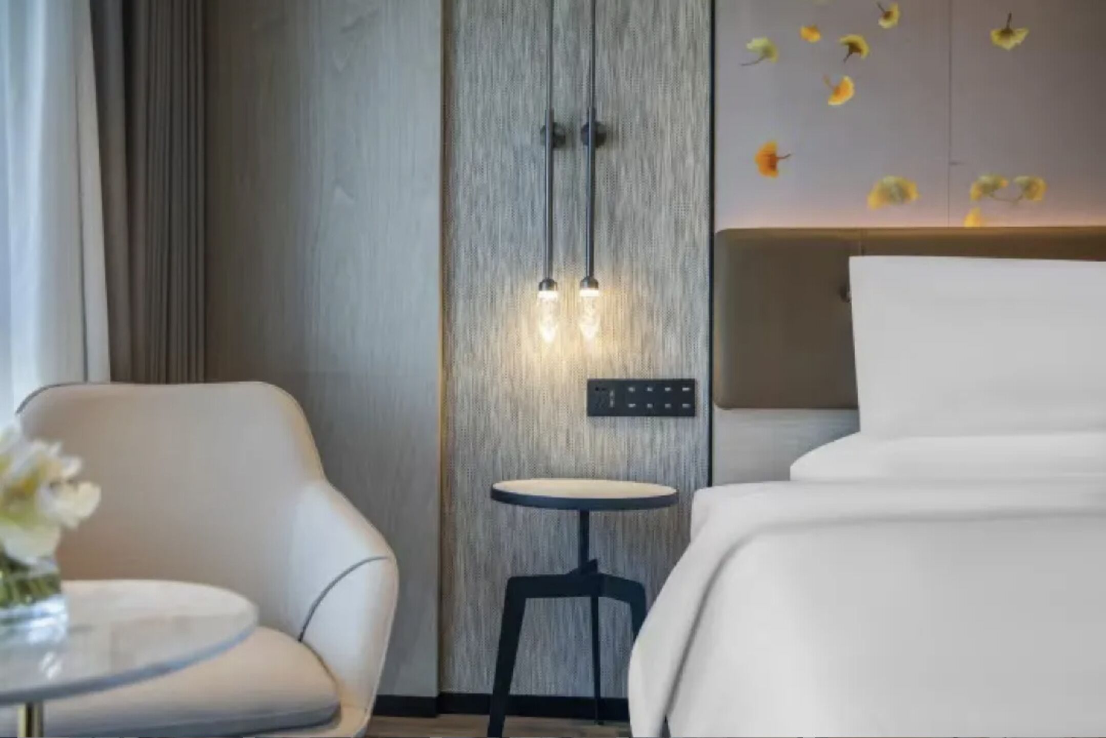 Habitación de hotel con cama, una silla, una mesita redonda e iluminación en la pared.