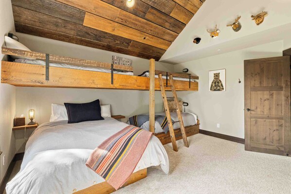 A bunk bed room with a ladder, a wooden ceiling, and a door.