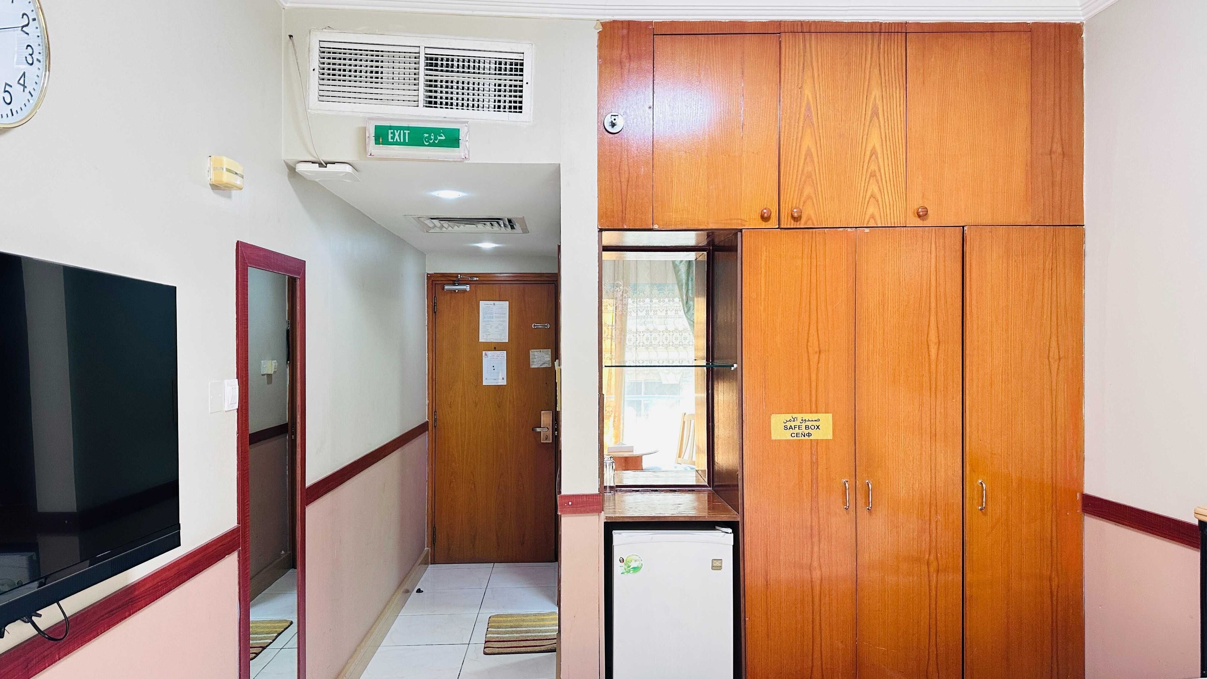 A hallway with a television, an exit sign, a safe box, and a refrigerator.