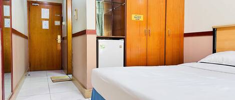 Habitación de hotel con cama, armario, refrigerador y una puerta con señal de caja fuerte.