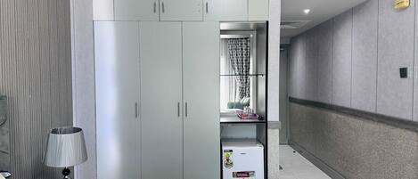 A hotel room with a wardrobe, a bedside table with a lamp, and a minibar.