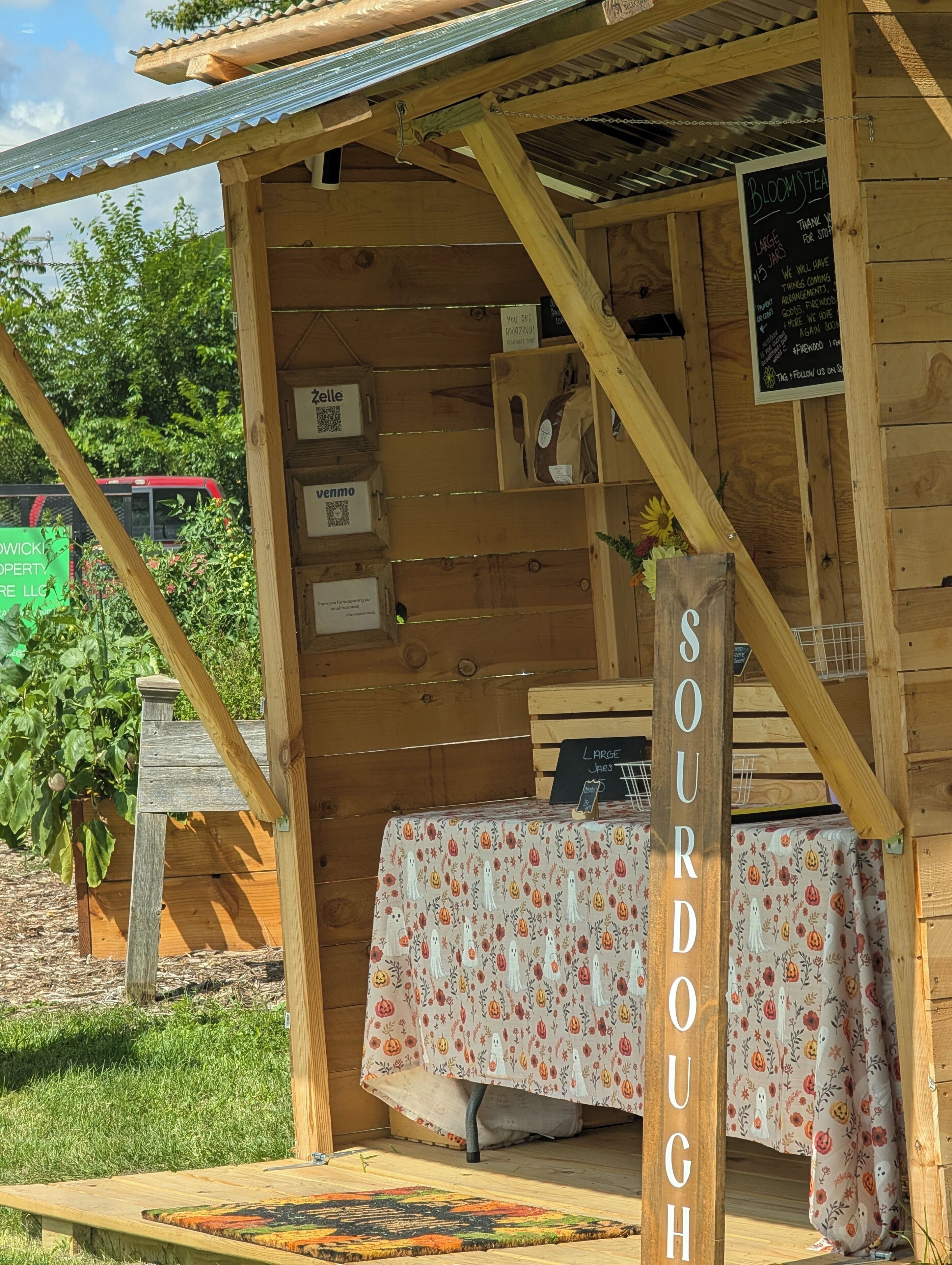 Eine rustikale Holzkonstruktion mit einem Tisch, bedeckt mit einer blumigen Tischdecke, auf dem 'SOURDOUCH' steht.