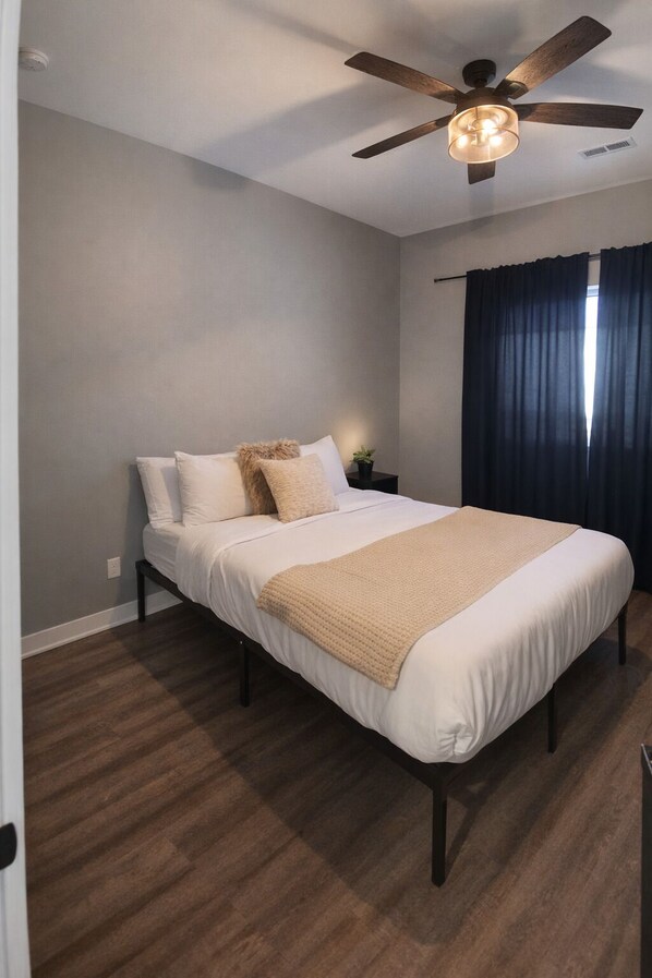 Un dormitorio con cama, ventilador de techo, mesita de noche y ventana con cortinas.