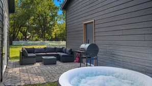 En udendørs terrasse med grå møbler, grill og jacuzzi.