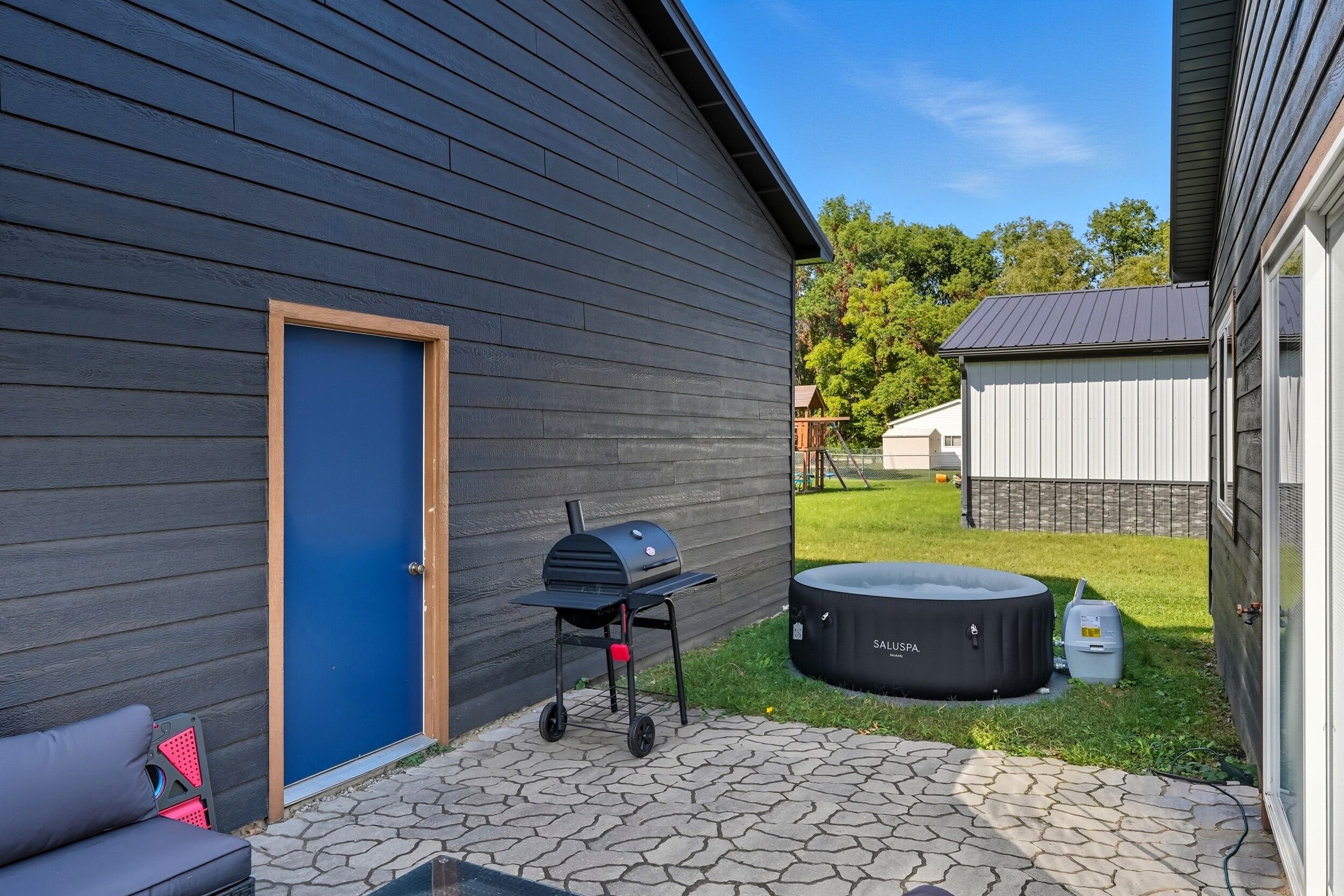 A patio with a grill, a blue door, and a hot tub.
