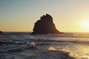A coastal scene with a prominent rock formation in the sea, waves crashing around it, and the sun setting in the background. - Sintra Farm Villa Guest House (Sintra)