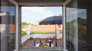 A balcony with a table, potted plants, and a view of a building with a tiled roof. - Sintra Farm Villa Guest House (Sintra)