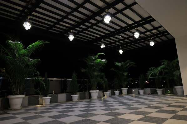 Un sol à carreaux, agrémenté de plantes en pot et illuminé par des lustres, le tout sous une zone abritée.