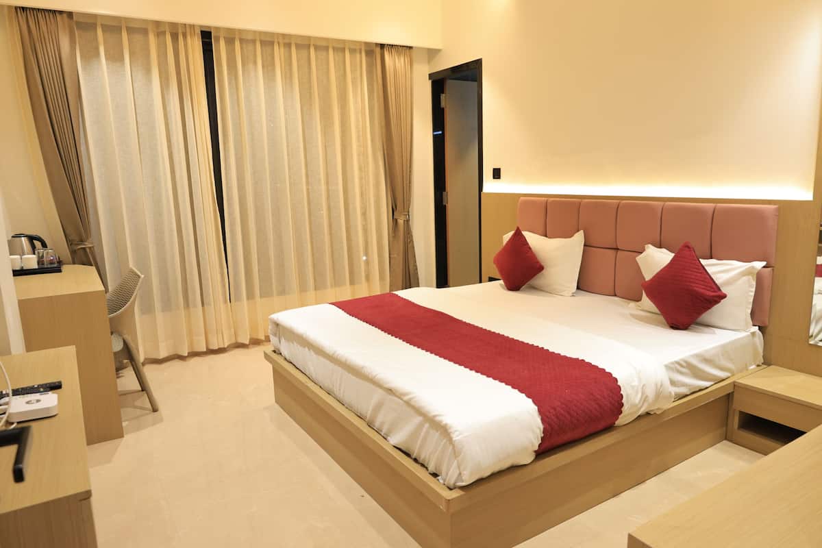 A hotel room with a large bed, a desk with a chair, and a wardrobe.