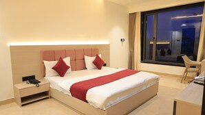 Moderni hotellihuone, jossa on suuri sänky, yöpöytä ja näkymä kaupunkiin yöllä.