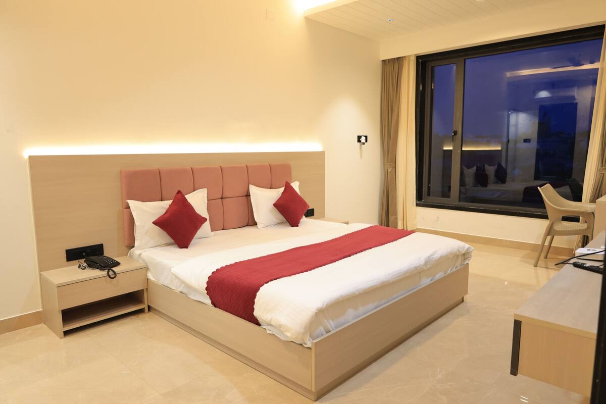 A modern hotel room with a large bed, bedside table, and a view of the city at night.