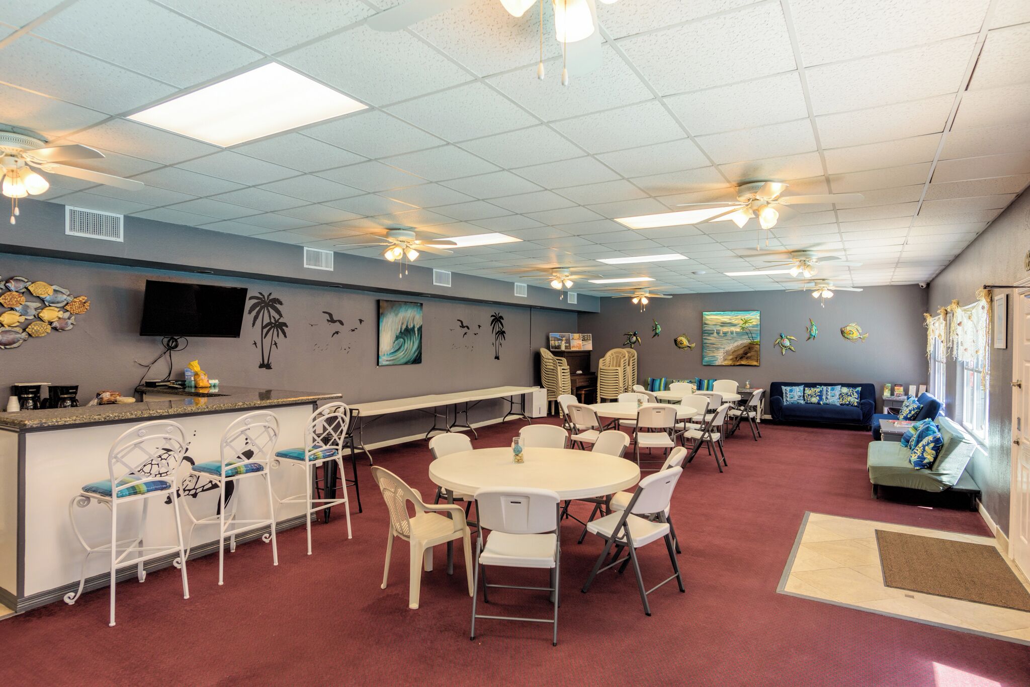 A spacious room with a long counter, multiple tables, and chairs, a television, and artwork on the walls.