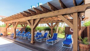 A wooden deck with blue lounge chairs under a pergola.