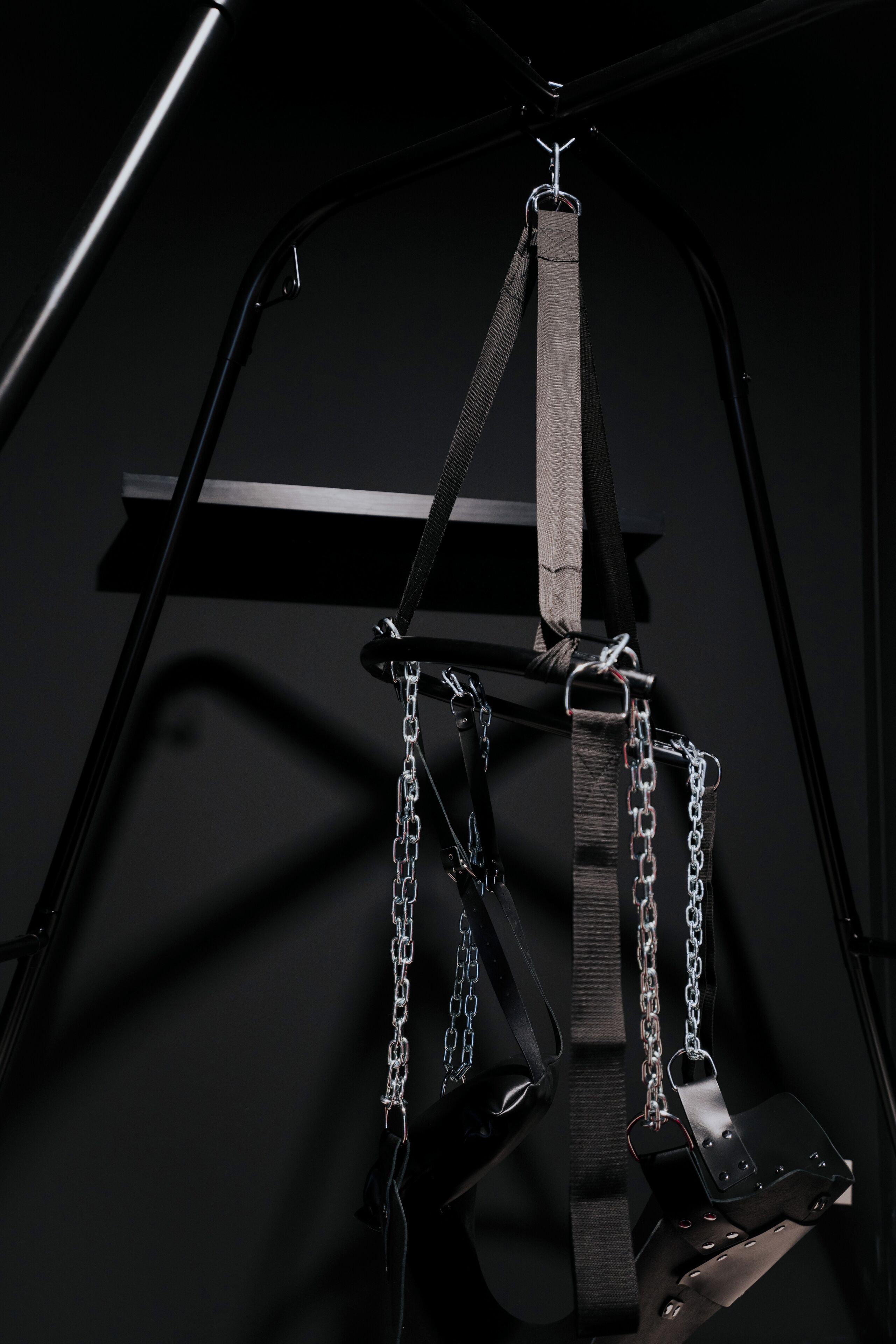 A black metal structure with chains and straps, likely part of a security or restraint system.