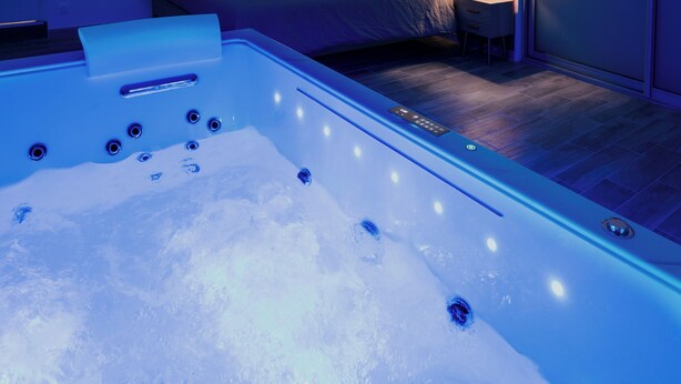 Una habitación de hotel moderna con una bañera grande, una cama con una mesita de noche y un armario.