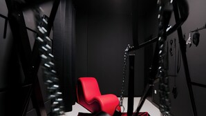 Una silla roja colgada por cadenas en una habitación con una paleta de colores blanco y negro.