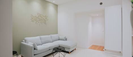 A modern living room with a light grey sectional sofa, a round coffee table, and a wall-mounted abstract art piece.