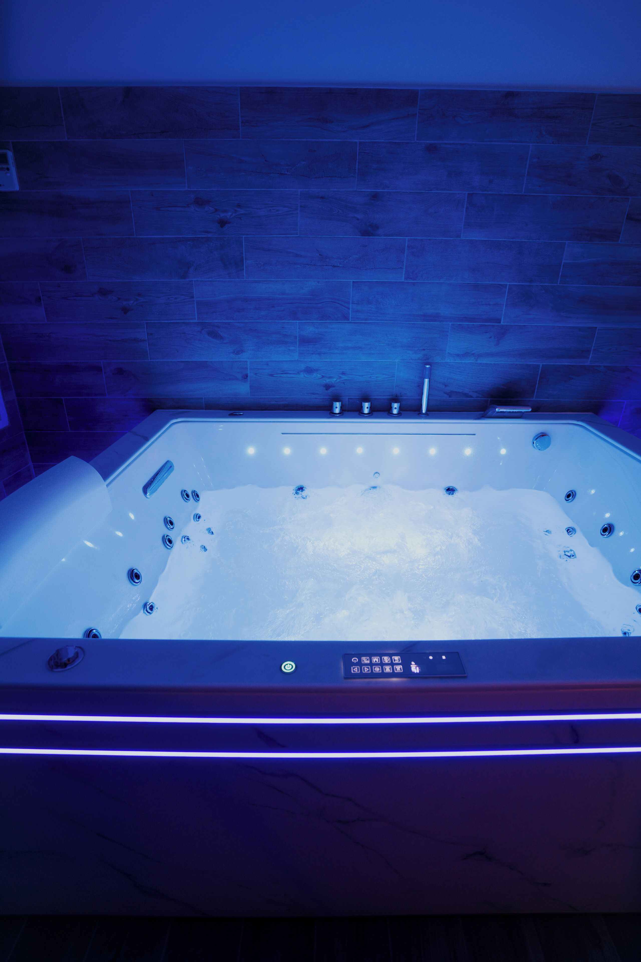 Une salle de bain moderne avec une baignoire sur pieds, un panneau de commande et un mur en bois.