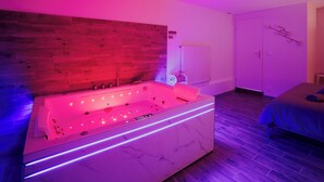 Un baño moderno con bañera de mármol, pared de madera y una cama en la habitación contigua.