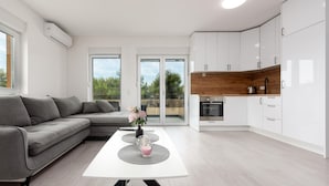 A modern kitchen with white cabinets and a wooden countertop, a grey sofa, and a dining table with a vase of flowers. - Cozy apartment in Vir with outdoor swimming pool (Vir)
