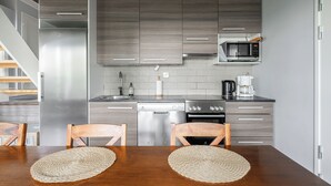 A modern kitchen with grey cabinetry, stainless steel appliances, and a wooden dining table with woven placemats. - Peaceful 2BR Getaway Cabin at Riihivuori (Muurame)