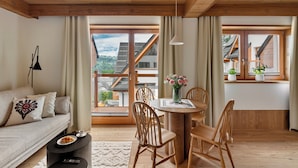 A cozy living room with a sofa, a dining table with chairs, and a view of a mountain through large windows. - IJG Imperial Smrekowa (Zakopane)